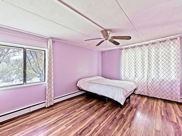 bedroom featuring a ceiling fan, baseboard heating, and wood finished floors