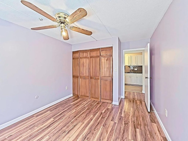 unfurnished bedroom featuring a closet, a textured ceiling, baseboards, ceiling fan, and light wood-style floors