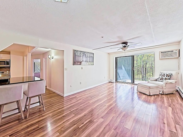living room with ceiling fan, a textured ceiling, a wall mounted air conditioner, and wood finished floors