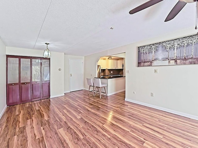 unfurnished living room with ceiling fan, a textured ceiling, baseboards, and wood finished floors