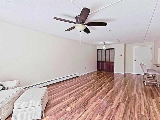 living area featuring baseboard heating, a textured ceiling, baseboards, ceiling fan, and wood finished floors