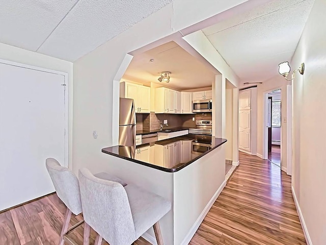 kitchen featuring baseboards, a sink, wood finished floors, dark countertops, and stainless steel appliances