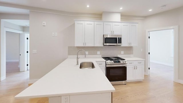 kitchen with appliances with stainless steel finishes, backsplash, sink, white cabinets, and light hardwood / wood-style floors