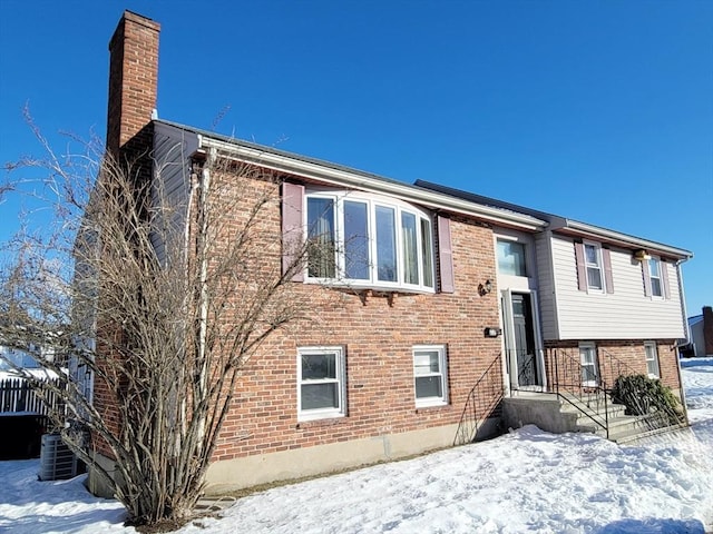 bi-level home with a chimney, cooling unit, and brick siding