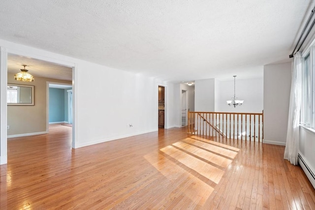 unfurnished room featuring baseboard heating, a textured ceiling, an inviting chandelier, and light hardwood / wood-style flooring