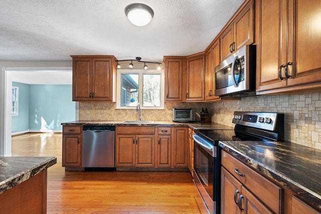 kitchen with sink, dark stone countertops, backsplash, stainless steel appliances, and light hardwood / wood-style flooring