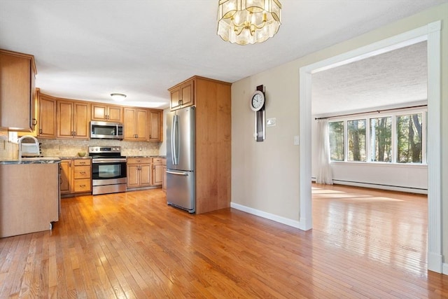 kitchen with sink, baseboard heating, appliances with stainless steel finishes, light hardwood / wood-style floors, and decorative backsplash