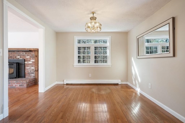 unfurnished dining area with hardwood / wood-style floors, a wood stove, a chandelier, and baseboard heating