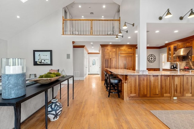 kitchen featuring brown cabinetry, light stone countertops, and under cabinet range hood