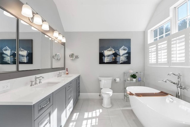 full bath with double vanity, tile patterned flooring, vaulted ceiling, a freestanding bath, and a sink