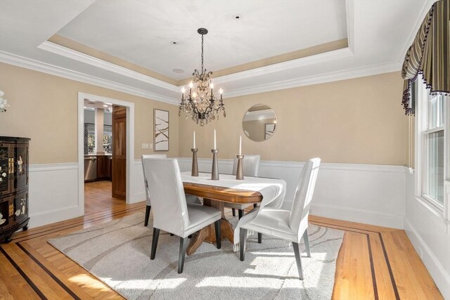 dining room with light wood-type flooring, a tray ceiling, a wealth of natural light, and wainscoting