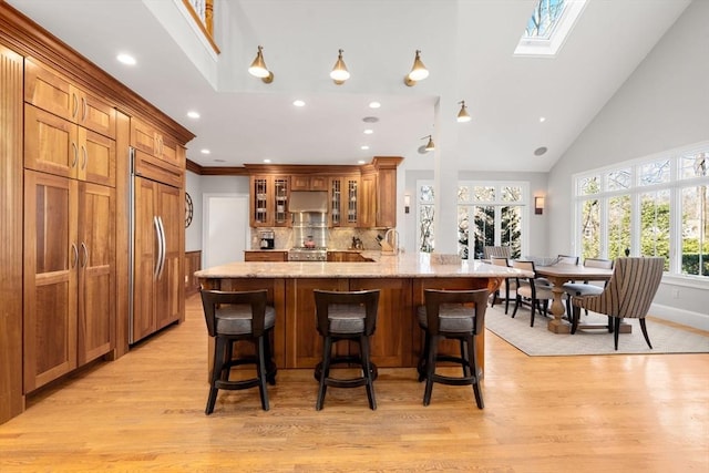 kitchen with a skylight, brown cabinets, paneled refrigerator, under cabinet range hood, and a kitchen breakfast bar