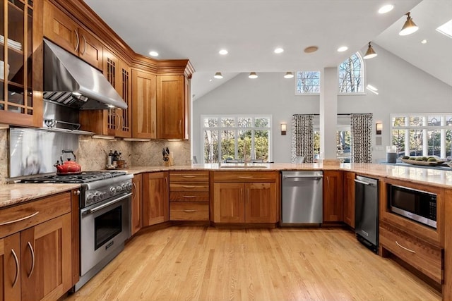 kitchen with range hood, appliances with stainless steel finishes, brown cabinetry, and light stone counters