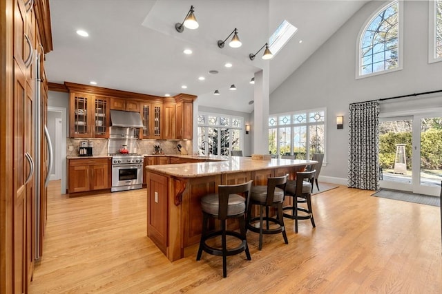 kitchen featuring brown cabinetry, a breakfast bar, high end range, a peninsula, and under cabinet range hood