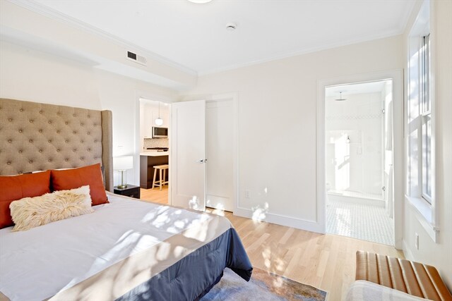 bedroom featuring ensuite bath, multiple windows, and light wood-type flooring