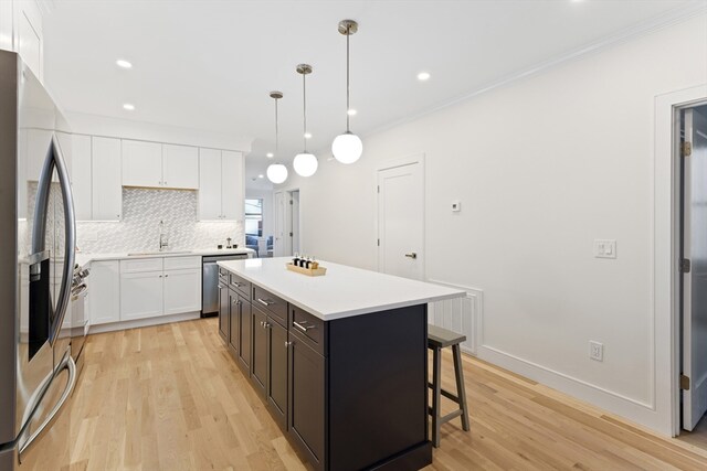 kitchen with white cabinetry, hanging light fixtures, stainless steel appliances, a kitchen island, and light wood-type flooring