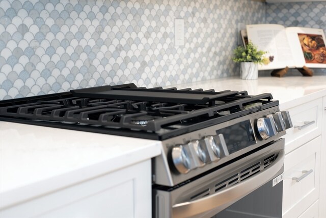 details with white cabinets, gas range, and backsplash