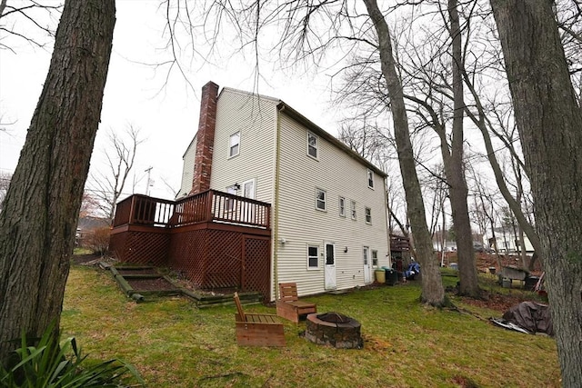 view of property exterior featuring an outdoor fire pit, a deck, a lawn, and a chimney