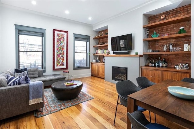 living room featuring a glass covered fireplace, light wood-style flooring, recessed lighting, and ornamental molding