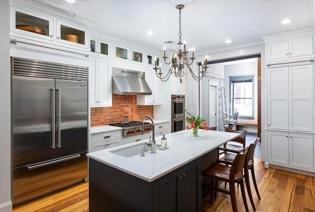 kitchen featuring light wood-style flooring, exhaust hood, white cabinets, stainless steel appliances, and a sink