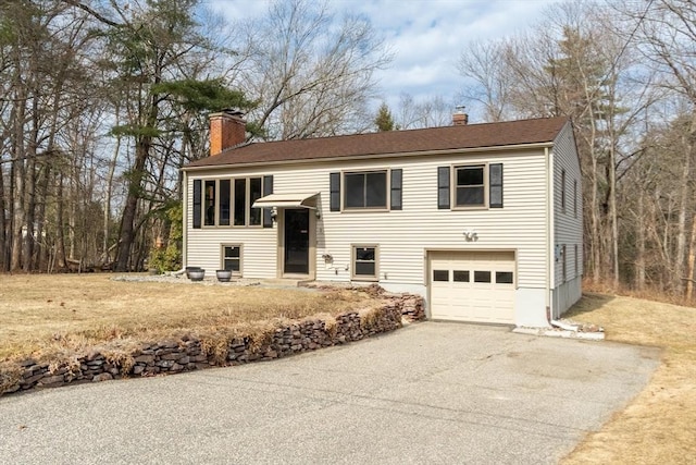 raised ranch featuring driveway, a chimney, an attached garage, and a shingled roof