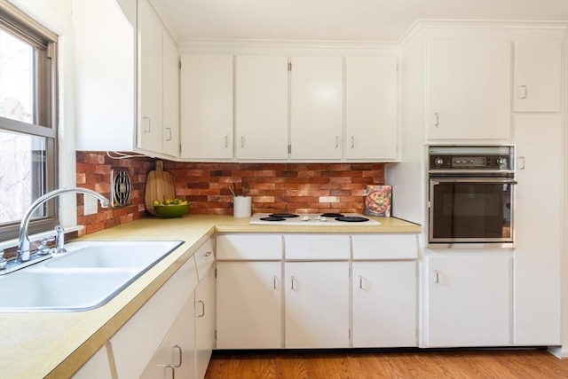 kitchen featuring a sink, oven, light countertops, light wood-style floors, and white electric cooktop