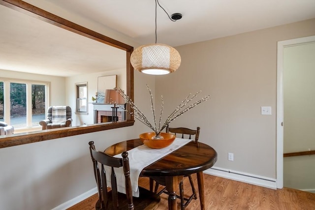 dining space with a baseboard radiator, baseboards, a brick fireplace, and wood finished floors