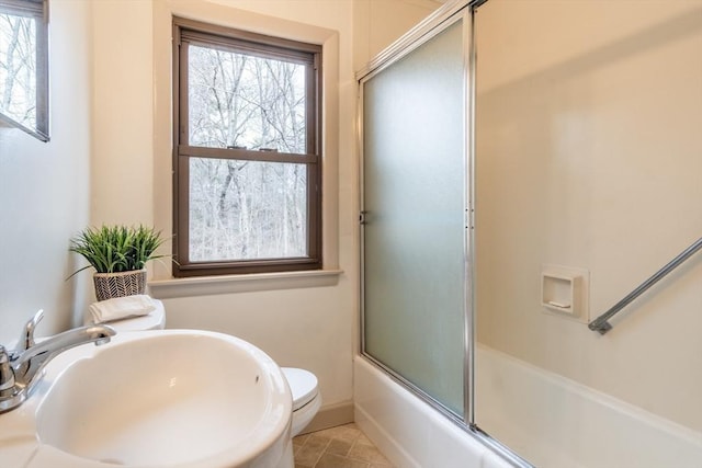 bathroom featuring toilet, baseboards, combined bath / shower with glass door, and a sink