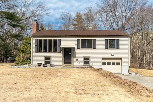 split foyer home with a garage, driveway, a front yard, and a chimney