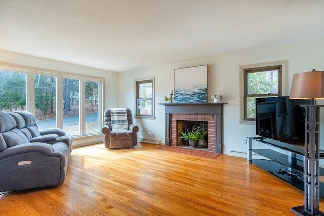 living room with a wealth of natural light, a brick fireplace, a baseboard heating unit, and wood finished floors