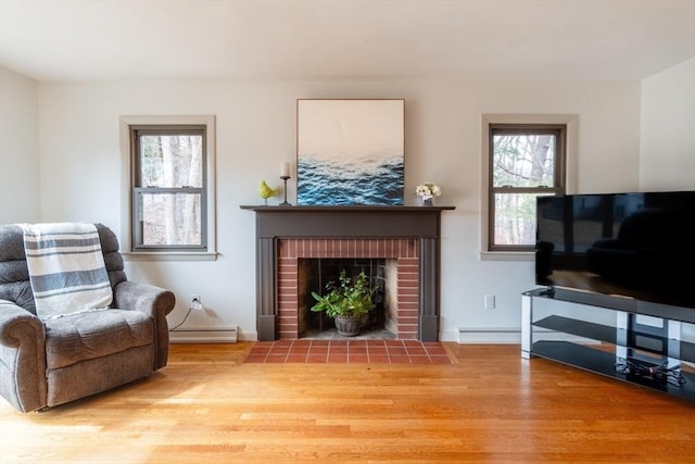 living room featuring wood finished floors, a brick fireplace, a healthy amount of sunlight, and baseboard heating