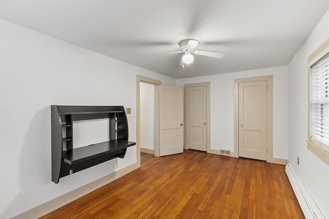 unfurnished living room featuring a ceiling fan, a baseboard radiator, baseboards, visible vents, and wood-type flooring