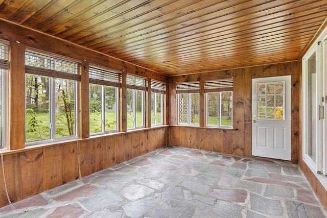 unfurnished sunroom with wooden walls, plenty of natural light, and stone flooring