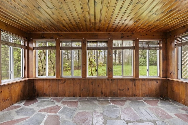 unfurnished sunroom featuring stone flooring, wood ceiling, wood walls, and a healthy amount of sunlight