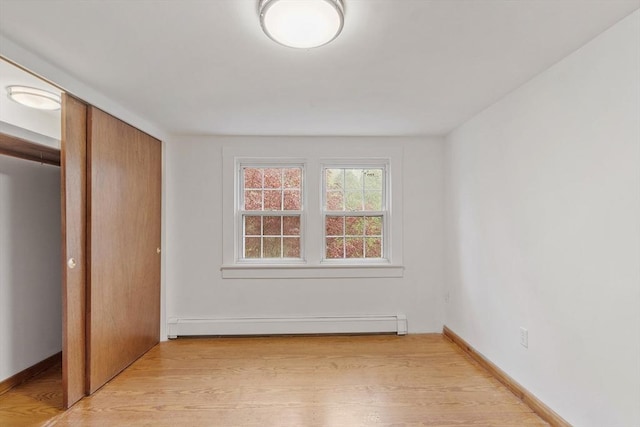 unfurnished bedroom featuring a closet, baseboards, baseboard heating, and light wood-style floors