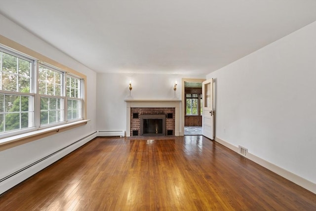 unfurnished living room with a wealth of natural light, a fireplace, a baseboard radiator, and wood-type flooring