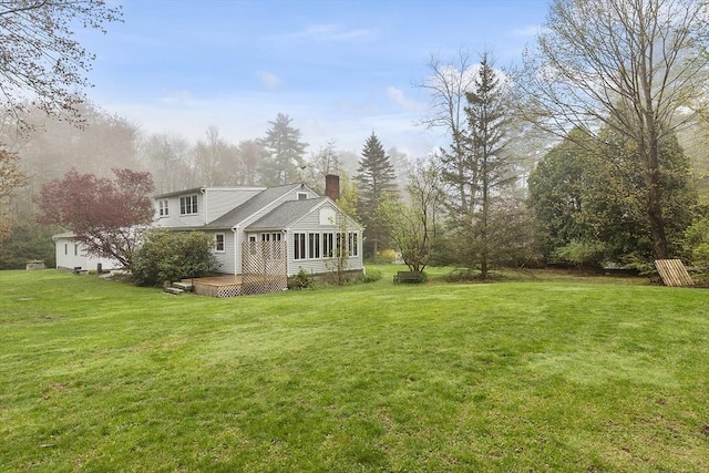 back of property featuring a chimney, a deck, and a yard
