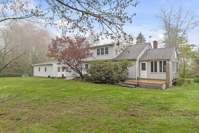back of house with a chimney, a wooden deck, a shingled roof, and a lawn
