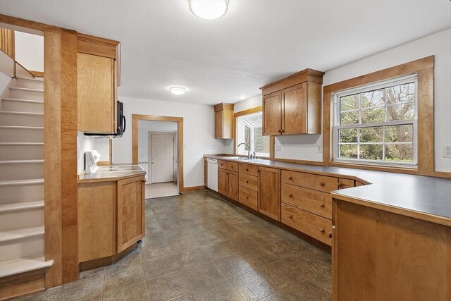 kitchen with a sink, brown cabinetry, light countertops, white dishwasher, and baseboards