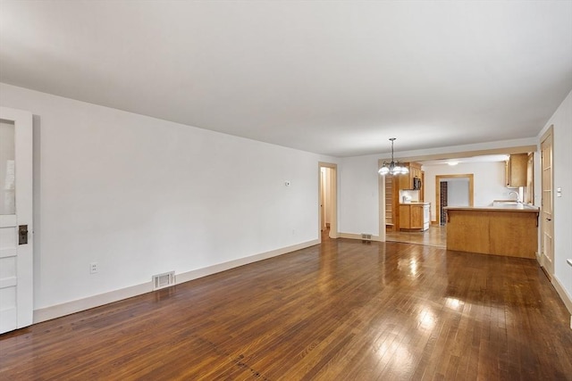 unfurnished living room with dark wood-type flooring, baseboards, visible vents, and a notable chandelier