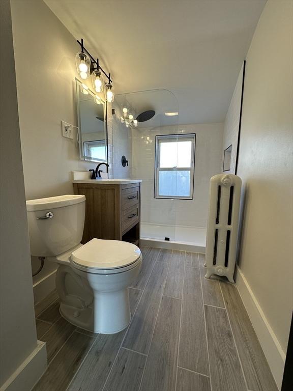 bathroom featuring vanity, baseboards, wood finish floors, a walk in shower, and toilet