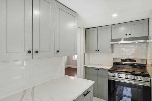 kitchen featuring tasteful backsplash, light stone countertops, under cabinet range hood, gas range, and gray cabinets