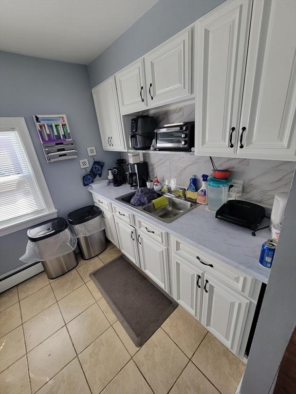 kitchen with a baseboard radiator, light tile patterned flooring, a sink, light countertops, and white cabinetry