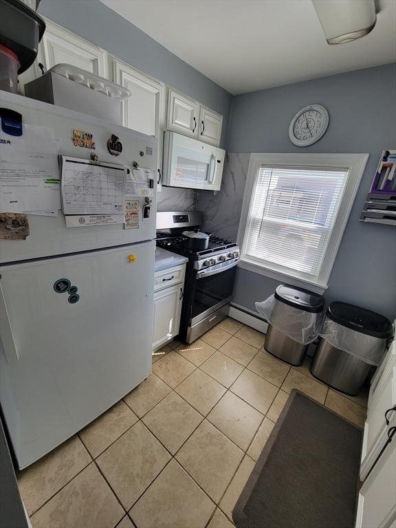 kitchen with white appliances, white cabinets, light countertops, light tile patterned floors, and baseboard heating