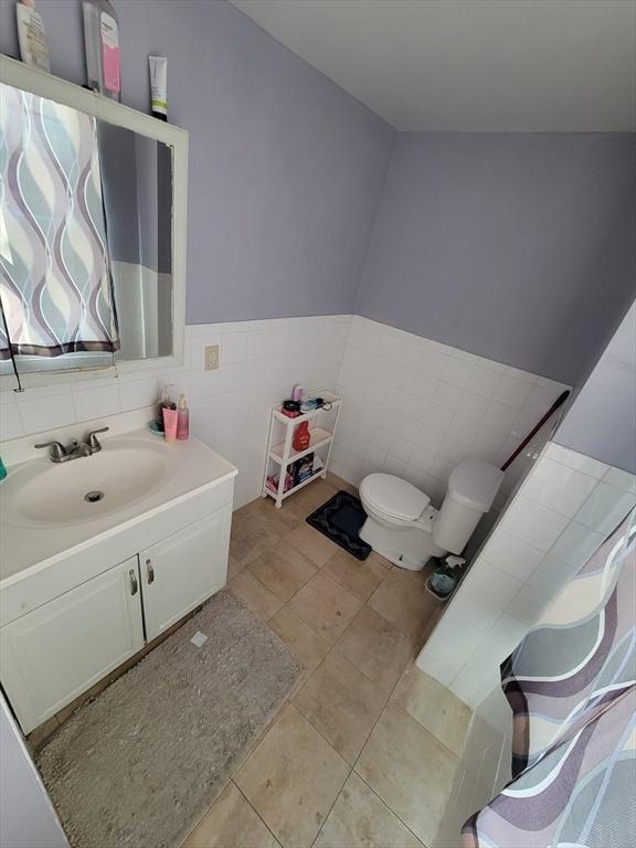 bathroom with toilet, vanity, wainscoting, tile patterned floors, and tile walls