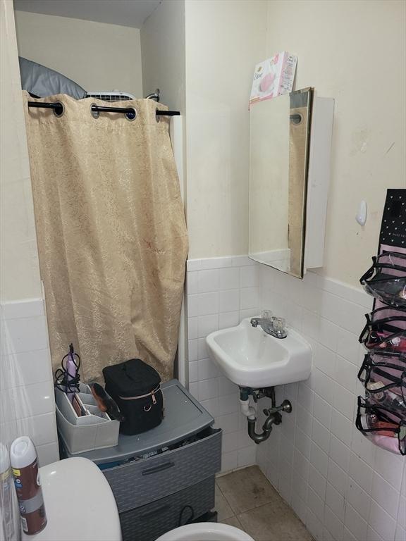 full bath featuring tile patterned flooring, tile walls, and a wainscoted wall