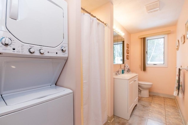 washroom with stacked washer and dryer, visible vents, light tile patterned flooring, laundry area, and baseboards