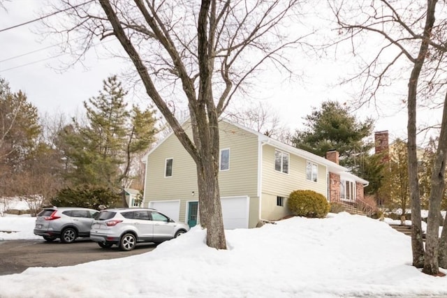 view of snow covered exterior featuring a garage and a chimney