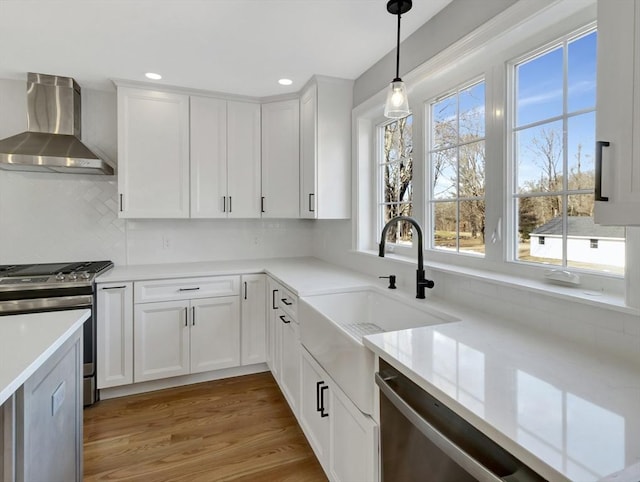 kitchen with white cabinets, wall chimney exhaust hood, appliances with stainless steel finishes, and a sink