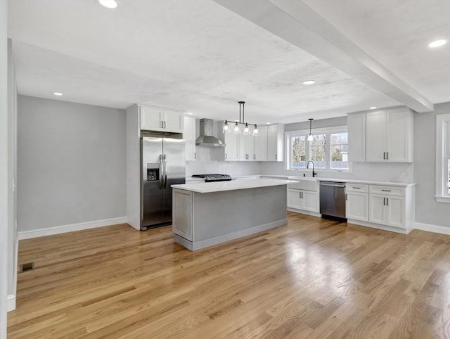 kitchen with baseboards, wall chimney range hood, light countertops, appliances with stainless steel finishes, and light wood-style floors